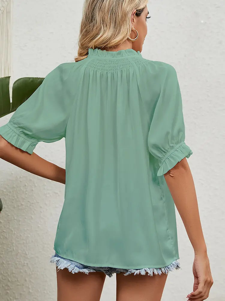Woman wearing a light green blouse with ruffled sleeves and hem.