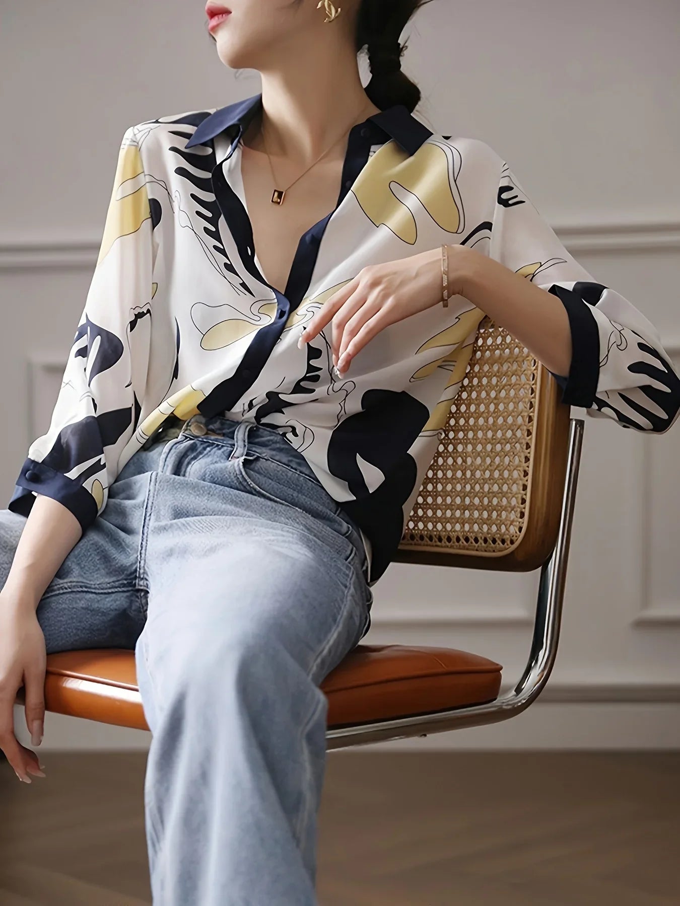 Person wearing a patterned shirt and jeans sitting on a chair indoors.