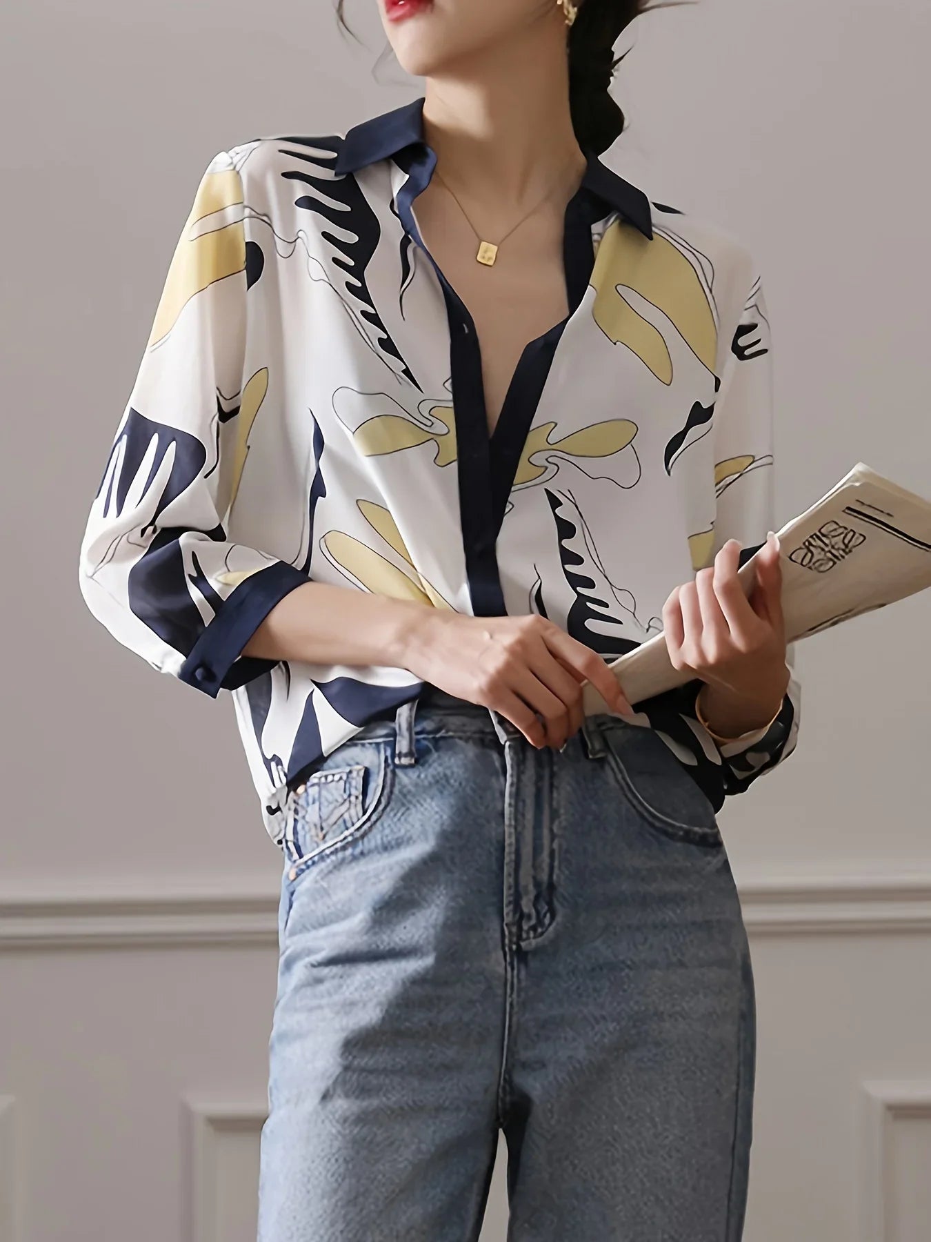 Person wearing a patterned blouse and jeans holding a book.